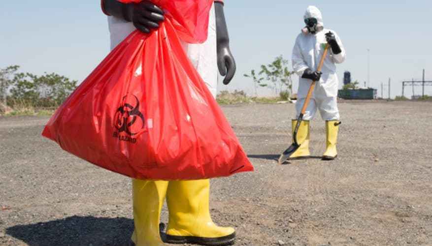 Two people in protective bio-hazard gear with a shovel and disposal bag