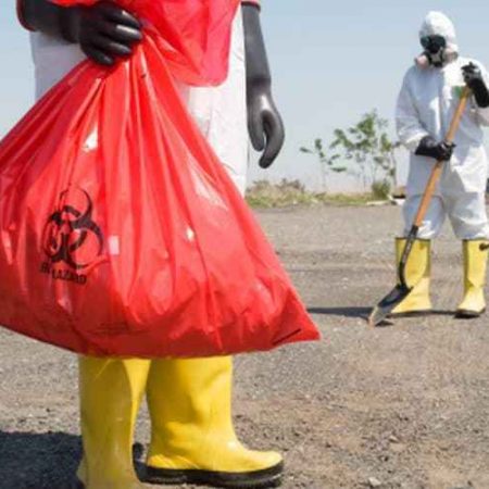 Two people in protective bio-hazard gear with a shovel and disposal bag